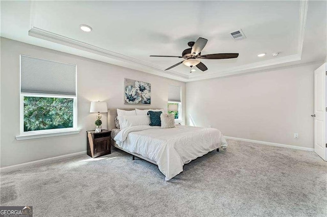 carpeted bedroom featuring baseboards, visible vents, a raised ceiling, and crown molding