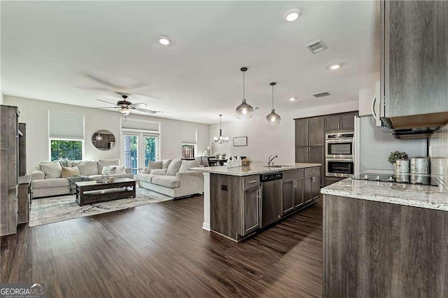 kitchen with dark brown cabinetry, stainless steel appliances, a sink, open floor plan, and a center island with sink