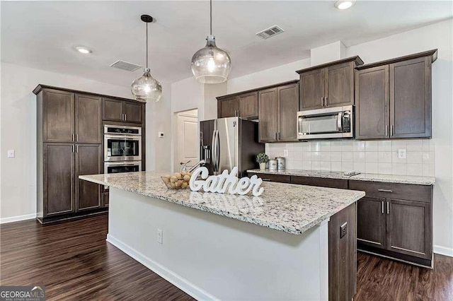 kitchen featuring light stone counters, visible vents, appliances with stainless steel finishes, an island with sink, and decorative light fixtures