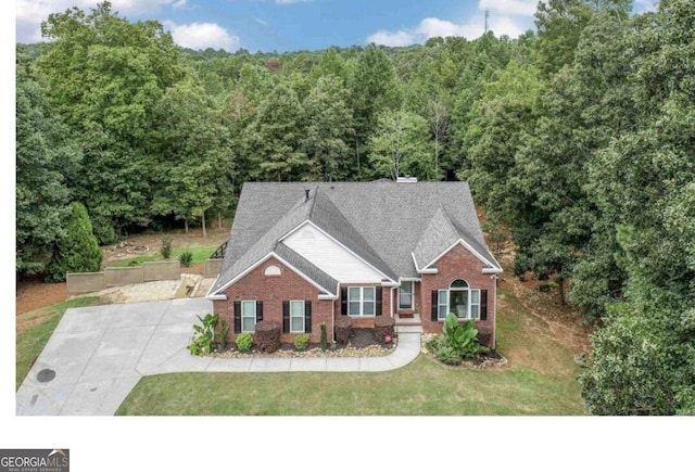 view of front of property featuring brick siding, a front lawn, and a wooded view