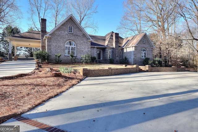 view of front of home featuring a carport, driveway, brick siding, and a chimney