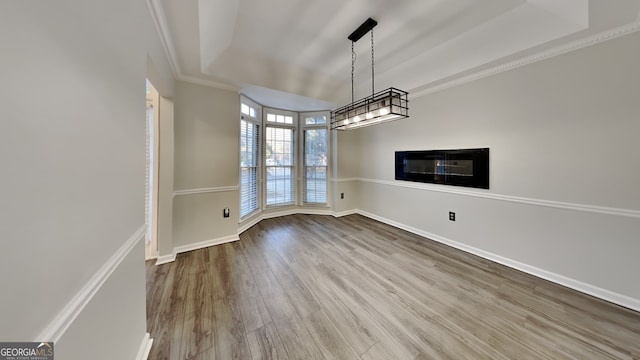 unfurnished dining area with light wood finished floors, a tray ceiling, baseboards, and crown molding