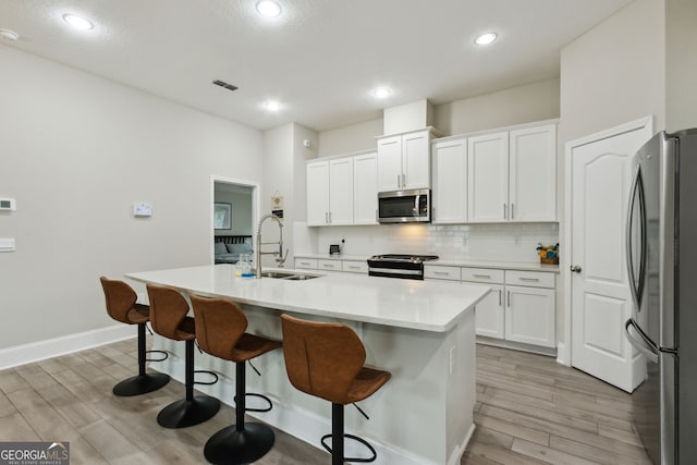 kitchen featuring stainless steel appliances, white cabinets, a kitchen island with sink, and a sink