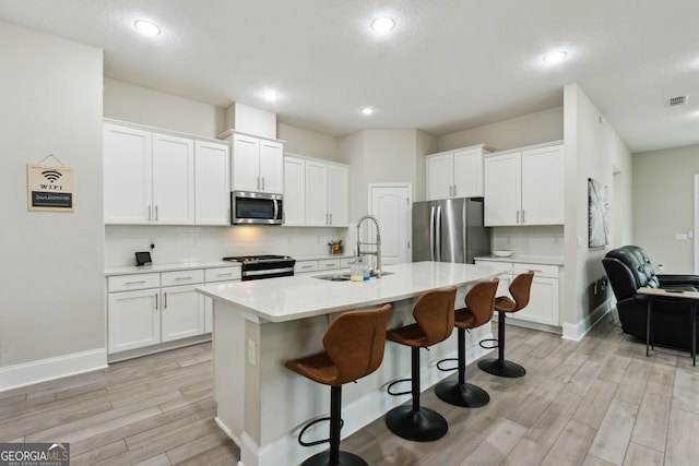 kitchen featuring white cabinets, appliances with stainless steel finishes, light countertops, and a sink