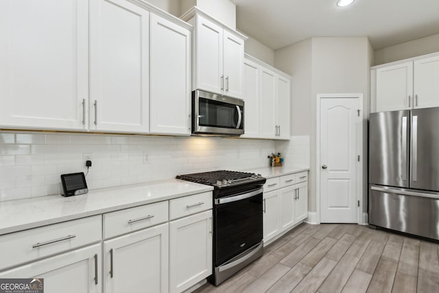 kitchen featuring stainless steel appliances, white cabinetry, and light stone counters