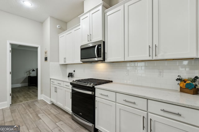 kitchen featuring light wood finished floors, stainless steel appliances, backsplash, white cabinetry, and light stone countertops