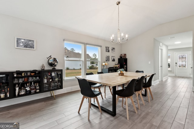 dining area with light wood-type flooring, a notable chandelier, lofted ceiling, and baseboards