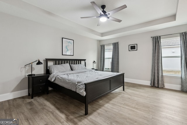 bedroom with a ceiling fan, a tray ceiling, light wood-style flooring, and baseboards