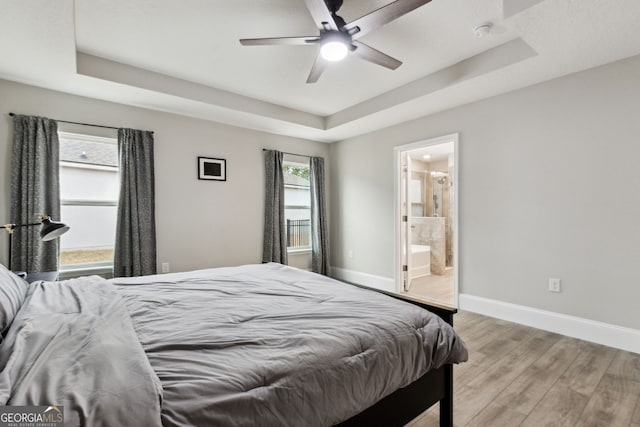 bedroom featuring ensuite bathroom, light wood-type flooring, a raised ceiling, and baseboards