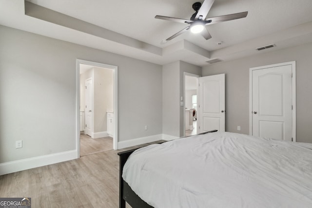 bedroom with a raised ceiling, visible vents, connected bathroom, light wood-type flooring, and baseboards