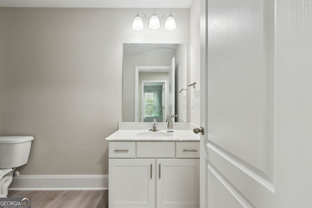 half bath with a textured wall, toilet, vanity, wood finished floors, and baseboards