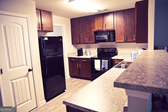 kitchen with a sink, visible vents, light countertops, black appliances, and light wood finished floors