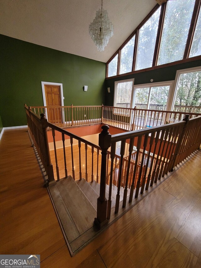 stairway featuring baseboards, wood finished floors, a notable chandelier, high vaulted ceiling, and beam ceiling