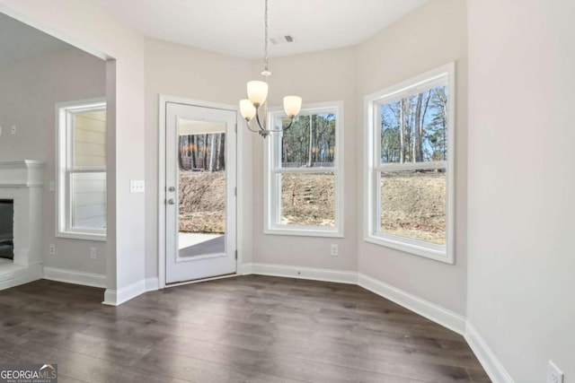 unfurnished dining area featuring visible vents, baseboards, a brick fireplace, dark wood-style floors, and an inviting chandelier