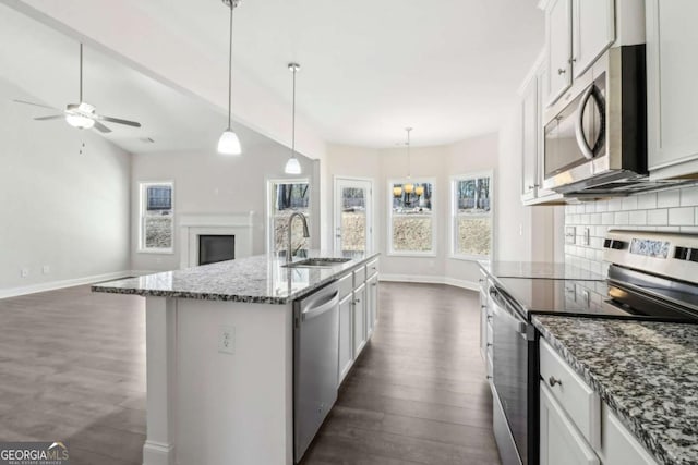 kitchen with stainless steel appliances, open floor plan, a kitchen island with sink, white cabinets, and a sink