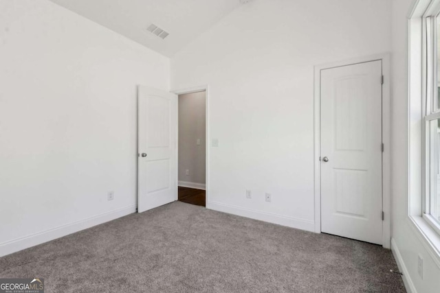 unfurnished bedroom with lofted ceiling, baseboards, visible vents, and light colored carpet