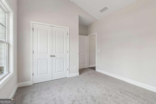 unfurnished bedroom featuring multiple windows, visible vents, a closet, and light colored carpet