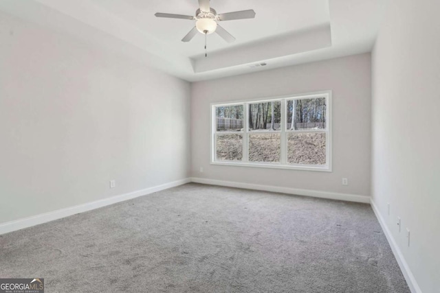 carpeted empty room featuring baseboards, a tray ceiling, and ceiling fan