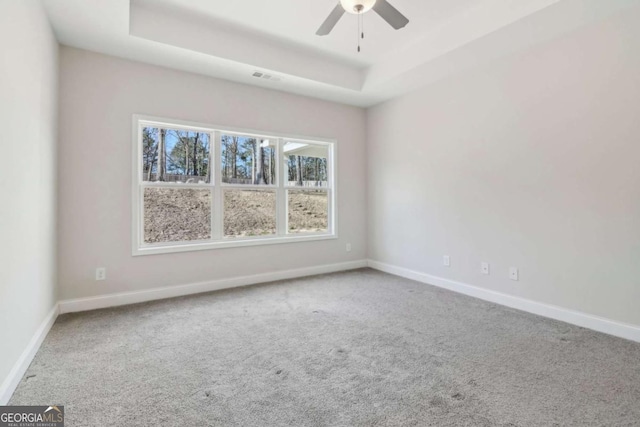 empty room with carpet floors, a tray ceiling, visible vents, and baseboards