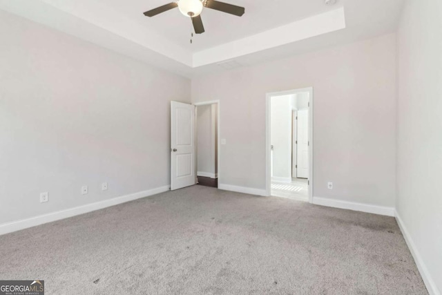 unfurnished bedroom with a tray ceiling, light colored carpet, ceiling fan, and baseboards