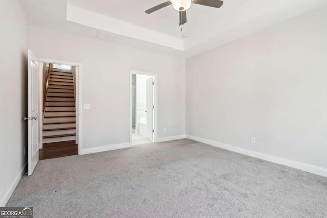 unfurnished bedroom featuring baseboards, a raised ceiling, a ceiling fan, and light colored carpet