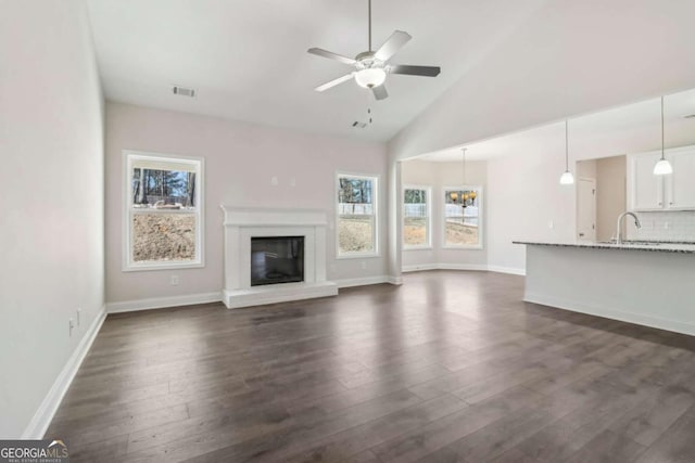 unfurnished living room with ceiling fan with notable chandelier, dark wood finished floors, a sink, and a glass covered fireplace