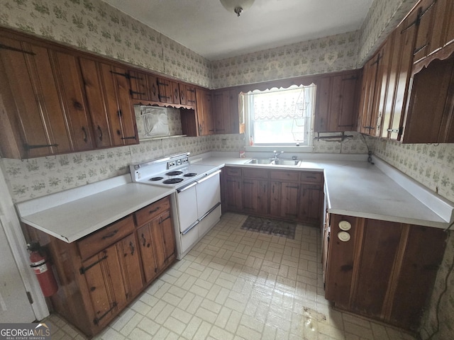 kitchen featuring wallpapered walls, white range with electric stovetop, light countertops, and a sink