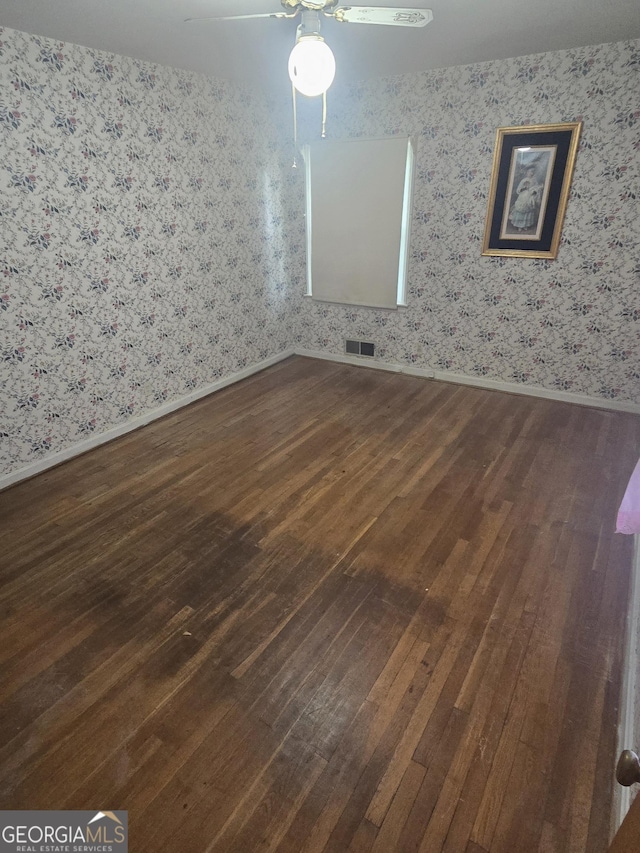 unfurnished room featuring dark wood-style floors, visible vents, and wallpapered walls