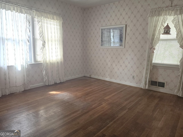 spare room featuring visible vents, dark wood finished floors, baseboards, and wallpapered walls