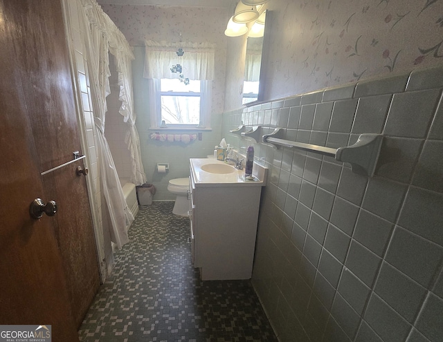 full bath with tile walls, toilet, wainscoting, vanity, and wallpapered walls