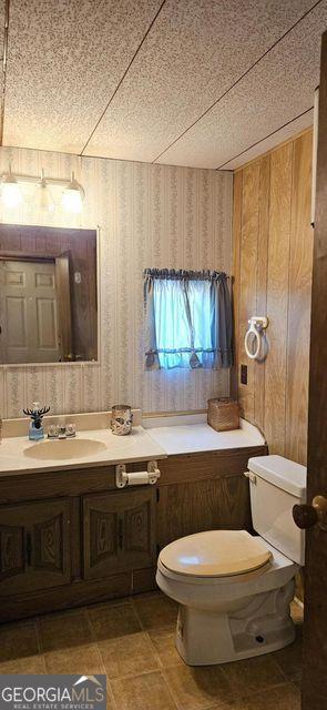 bathroom featuring toilet, wallpapered walls, and vanity