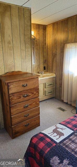 bedroom featuring light carpet, visible vents, and wooden walls