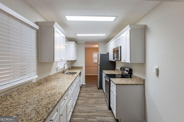 kitchen featuring appliances with stainless steel finishes, white cabinets, a sink, and light stone countertops