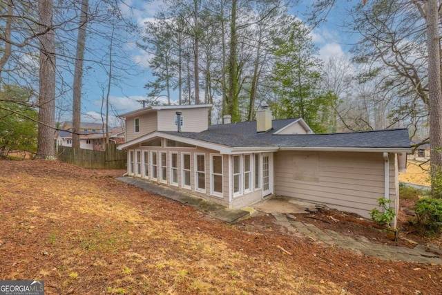 rear view of property featuring a shingled roof, a sunroom, fence, and a chimney