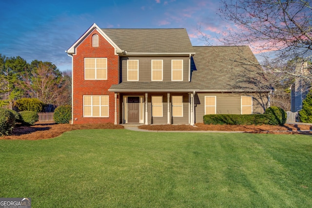 view of front of home featuring brick siding, fence, and a front lawn