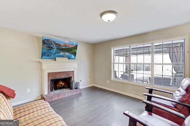 living room with dark wood-style flooring, a brick fireplace, and baseboards