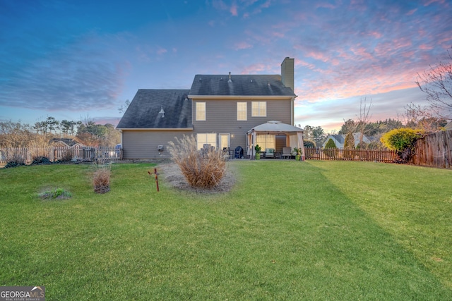 back of property featuring a fenced backyard, a chimney, a lawn, and a gazebo