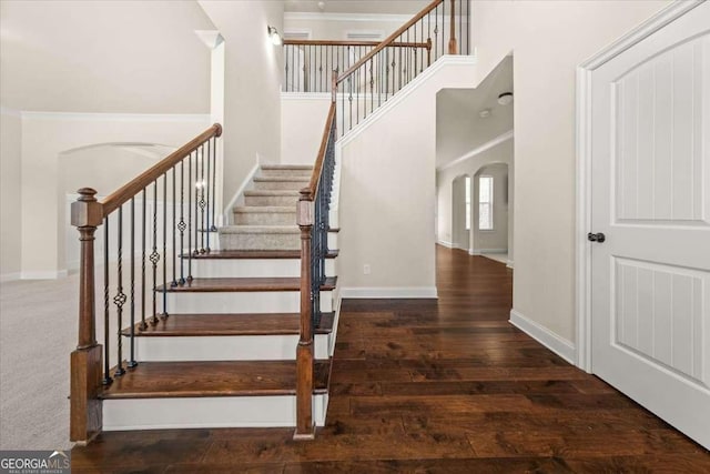 stairway featuring arched walkways, a towering ceiling, baseboards, and wood finished floors