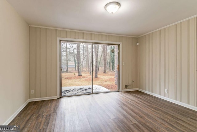 empty room with dark wood-style floors, crown molding, and baseboards