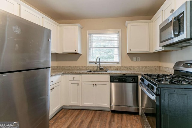 kitchen with dark wood finished floors, appliances with stainless steel finishes, light stone counters, white cabinetry, and a sink