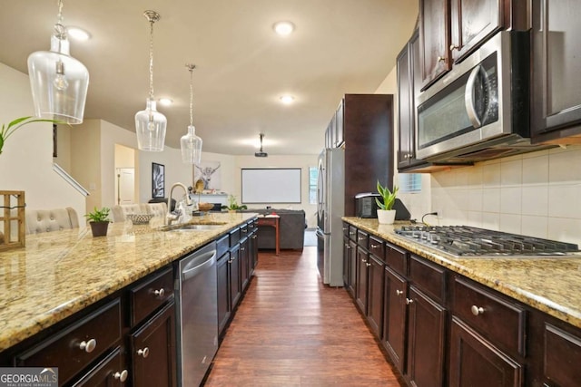 kitchen with light stone counters, a sink, hanging light fixtures, appliances with stainless steel finishes, and dark wood finished floors