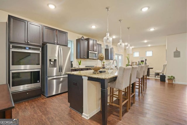 kitchen featuring a breakfast bar, a center island with sink, hanging light fixtures, appliances with stainless steel finishes, and light stone countertops