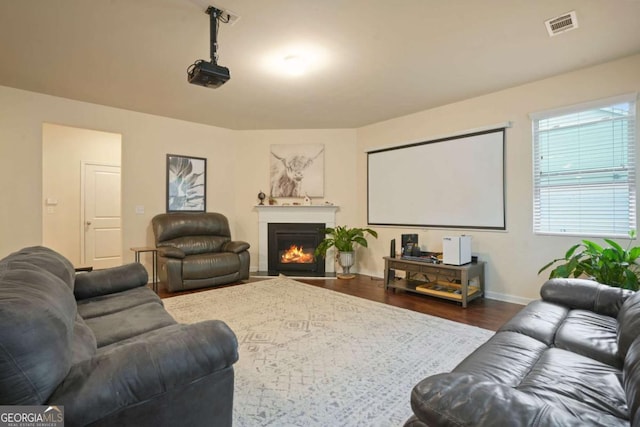 cinema room featuring a fireplace with flush hearth, visible vents, baseboards, and wood finished floors