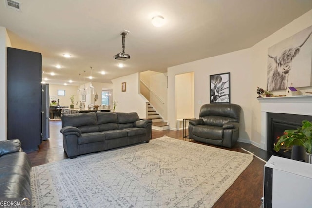 living room with dark wood-style flooring, a fireplace, visible vents, baseboards, and stairs