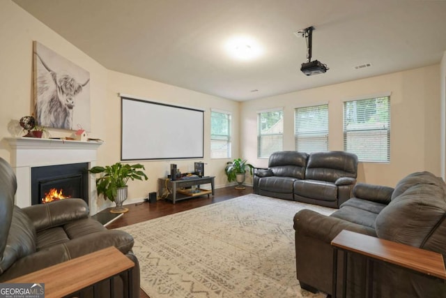 home theater featuring a warm lit fireplace, baseboards, visible vents, and dark wood finished floors