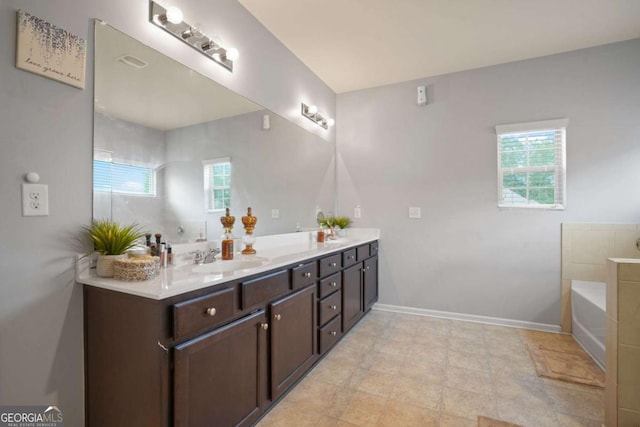 full bath with double vanity, a garden tub, baseboards, and a sink