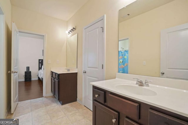 bathroom featuring ensuite bathroom, two vanities, a sink, visible vents, and baseboards