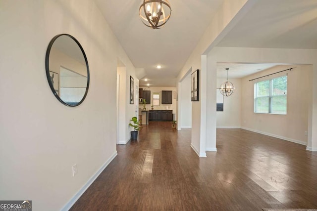 corridor featuring baseboards, dark wood finished floors, and a notable chandelier