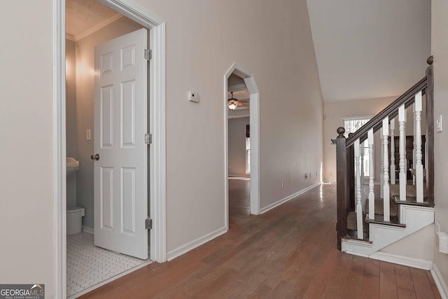 hallway featuring hardwood / wood-style floors, stairway, baseboards, lofted ceiling, and arched walkways