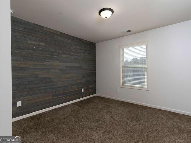 empty room with wooden walls, baseboards, visible vents, an accent wall, and dark carpet